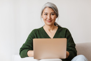 Image of adult asian woman using laptop computer on sofa at home