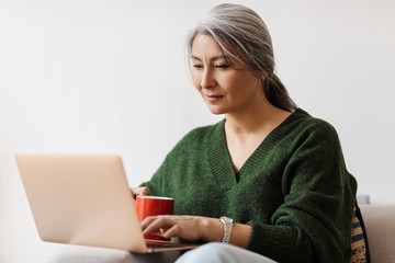 Image of beautiful adult asian woman using laptop computer at home