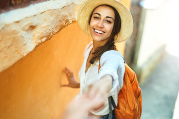 happy carefree tourist woman in straw hat, white shirt and orange backpack holding hand of her...
