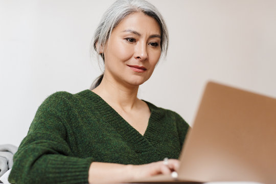 Image of adult asian woman using laptop computer on sofa at home