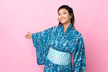 Young woman wearing kimono over isolated blue background extending hands to the side for inviting to come