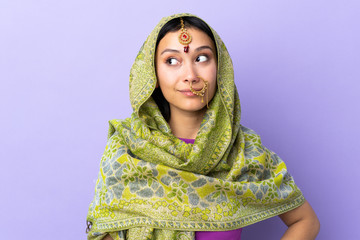 Indian woman isolated on purple background making doubts gesture looking side