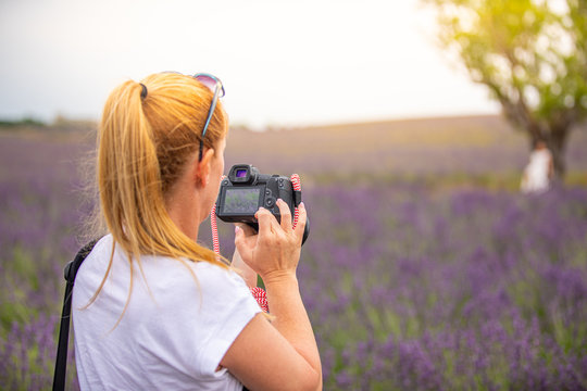 Beautiful woman taking picture outdoors with a DSLR camera. Young blonde woman, professional photographer, taking pictures of a beautiful nature surrounding her, warm sunny day in lavender field.