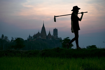 silhouette of farmer walks carry hoe to the rice fiels in the early morning, living life of Thai culture traditional life in Countryside, with temple pagoda in background