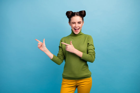 Photo Of Pretty Funny Lady Direct Finger Side Empty Space Offer Low Prices Shopping Flirty Wink Eye Wear Green Turtleneck Yellow Trousers Isolated Blue Color Background