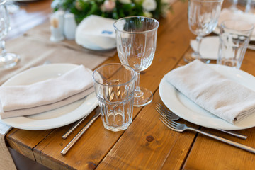 White napkin on a plate next to glasses, forks, knives, plates on a wooden table in the restaurant served for dinner. Set dining table in loft style