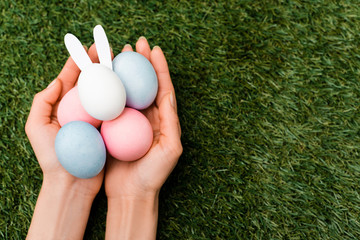 Cropped view of woman holding colorful chicken eggs and easter bunny on green background