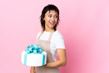 Uruguayan Pastry chef holding a big cake over isolated pink background laughing