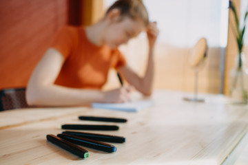 artist girl sitting at a wooden table draws on a background of a red wall 