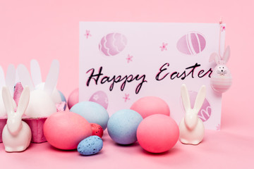 Colorful eggs, decorative bunnies and card with happy easter lettering on pink background