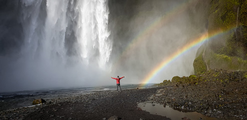Skogafoss waterfall with an unidentified man under the waterfall and a rainbow, Skogar, Iceland