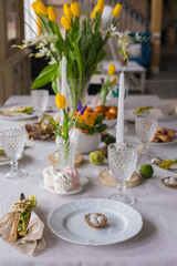 Easter festive spring table setting decoration, eggs in nest, fresh yellow tulips, marshmallows,...