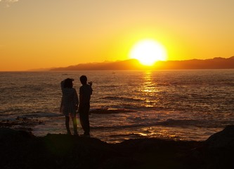 夕焼けの海に佇むカップルのシルエット