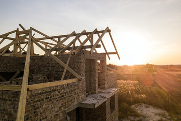 Private residential house with wooden roof frame structure under construction. Unfinished brick...