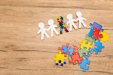 High angle view of special kid with autism among another and pieces of puzzle on wooden background