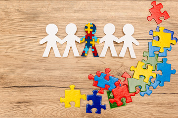 Top view of special kid with autism among another and pieces of bright colorful puzzle on wooden...