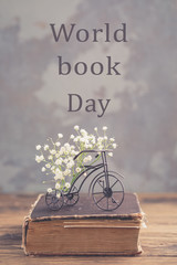 Old book, iron bicycle with flowers on wooden background, World Book Day concept, toned vintage,...