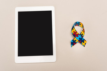 Top view of awareness ribbon and digital tablet on white background, autism concept