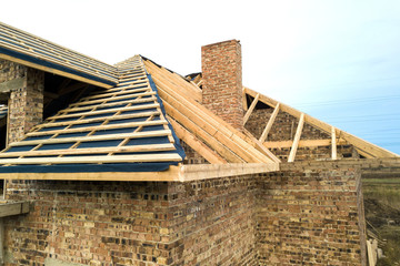 Private residential house with wooden roof frame structure under construction. Unfinished brick...