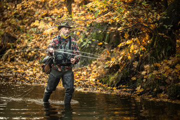 Handsome fisherman holding a lovely trout while  fly fishing on a splendid mountain river - obrazy, fototapety, plakaty