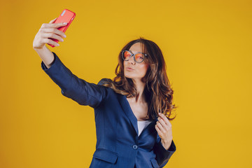 The elegantly dressed European woman raises her hand holding the phone to make a selfie, feels distracted and satisfied, has a beautiful smile.