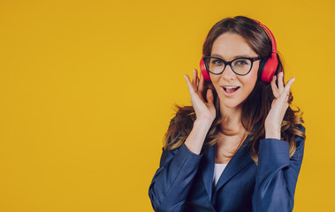 A girl wears busines and sexy, listens to music and smiles, on a yellow background. Place the text.
