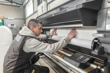 Technician operator changes paper roll on large printer plotter machine