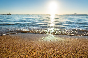 Close up of small sea waves with clear blue water over yellow sand beach at summer sunny shore.