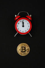 Bitcoin and red alarm clock on black background. Cryptocurrency concept. Gold Color coin.