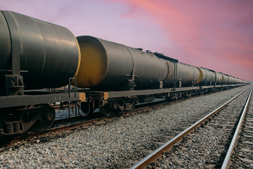 Black freight train wagons having oil tankers waiting on the rails againt sunrise sky