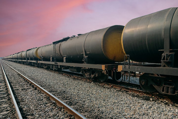 Fototapeta na wymiar Black freight train wagons having oil tankers waiting on the rails againt sunrise sky