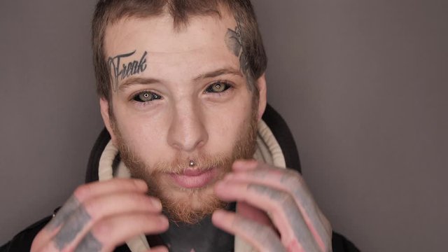 Close-up of a man with tattoo on his face and neck, eyeball or eye scleral tattooing, piercing, posing in studio, provocative aggressive look, Man demonstrating splitted tongue (body modification