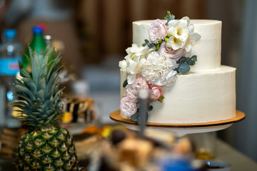 Tall sweet wedding cake decorated with live pink and white flowers on a table.