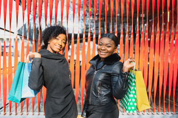 Two afro american women friends in the city on a shopping trip carrying colorful shopping bags.