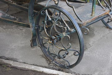 an iron decorative wheel with a forged pattern on a carriage stands on gray asphalt in the street