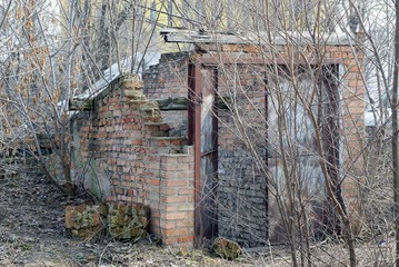 old ruined brown brick building with rusty iron door overgrown with dry vegetation on the street