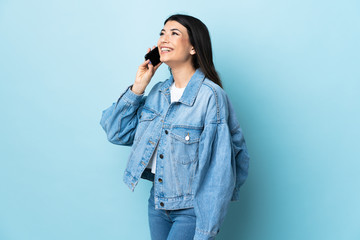 Young brunette girl over isolated blue background keeping a conversation with the mobile phone