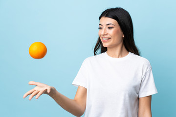 Young brunette girl over isolated blue background holding an orange