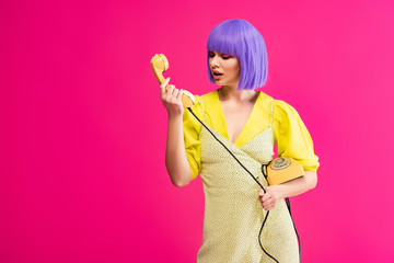 emotional woman in purple wig holding retro telephone, isolated on pink