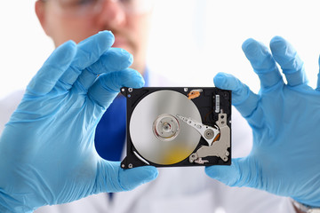 A male repairman wearing blue gloves is holding a hard drive from computer or laptop in hands....