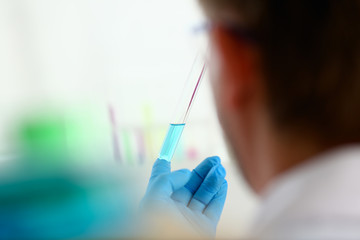 A male chemist holds test tube of glass in his hand overflows a liquid solution of potassium...