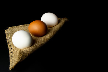 Three chicken eggs on a napkin, on black background