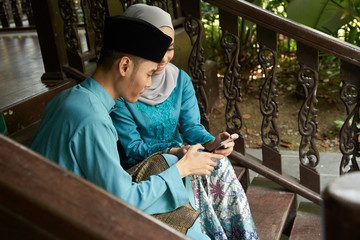 muslim couple with traditional clothing sitting at stair using mobile phone