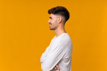 Young man over isolated orange background in lateral position