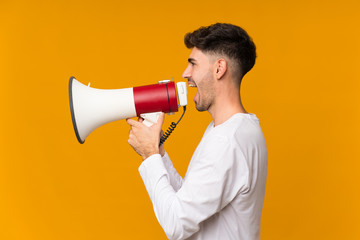 Young man over isolated orange background shouting through a megaphone
