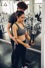 Attractive woman doing exercise with personal trainer at gym.