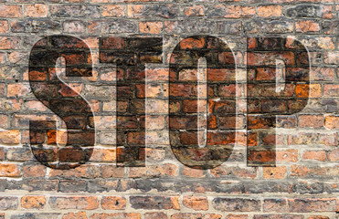 Brick wall of a ruined house in reddish and brown tones with the word Stop written in 3D.