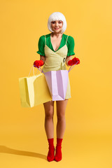 smiling pop art girl in white wig holding shopping bags, on yellow