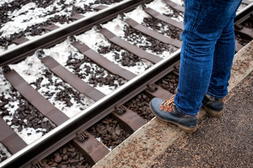 Woman standing waiting train at platform standing too close to the edge. Feet at railway station.