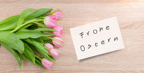 Rosarote Tulpen auf einem Holztisch mit Osterkarte "Frohe Ostern"